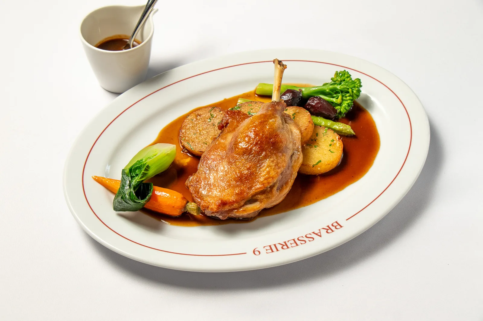 ขาเป็ดคอนฟีต์ เสิร์ฟกับมันฝรั่งสไลซ์ แครอท บรอกโคลี และซอสไวน์แดง บนจาน Brasserie 9 สาทร กรุงเทพฯ